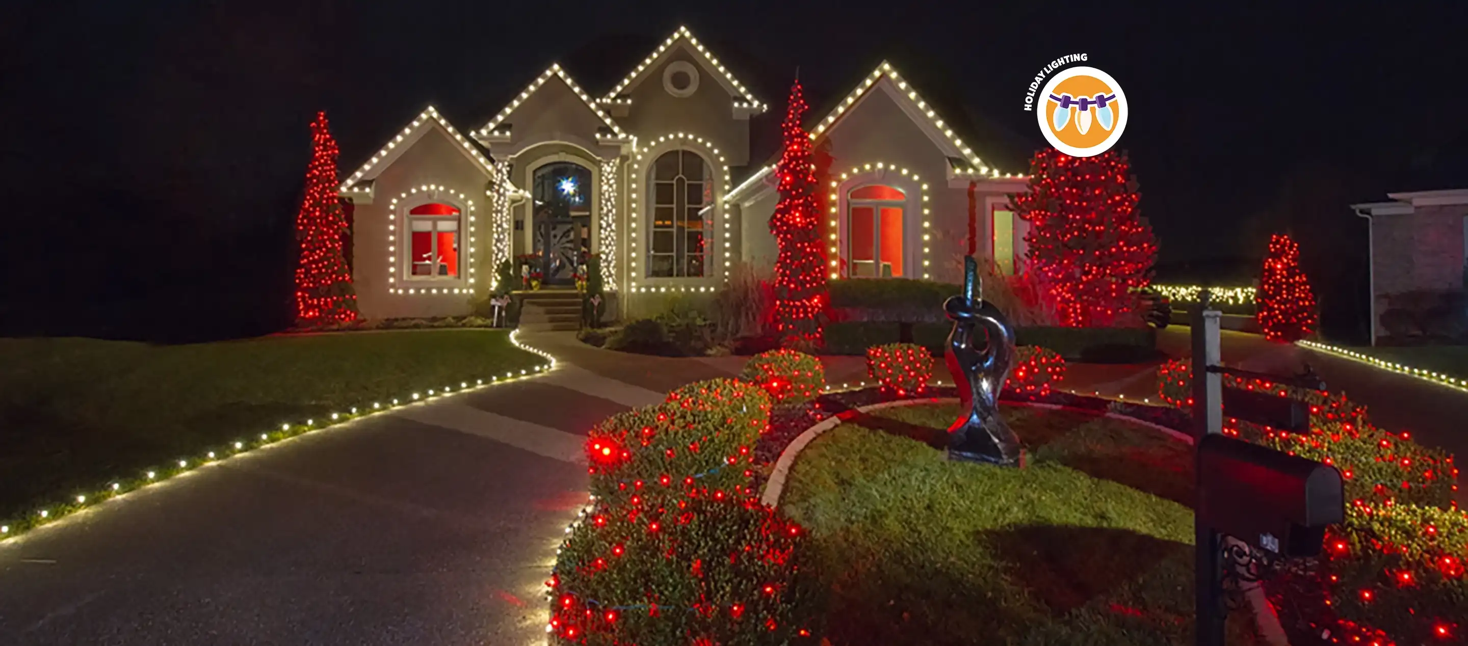 Large single-family home with wraparound driveway lit up by red and white holiday lights.