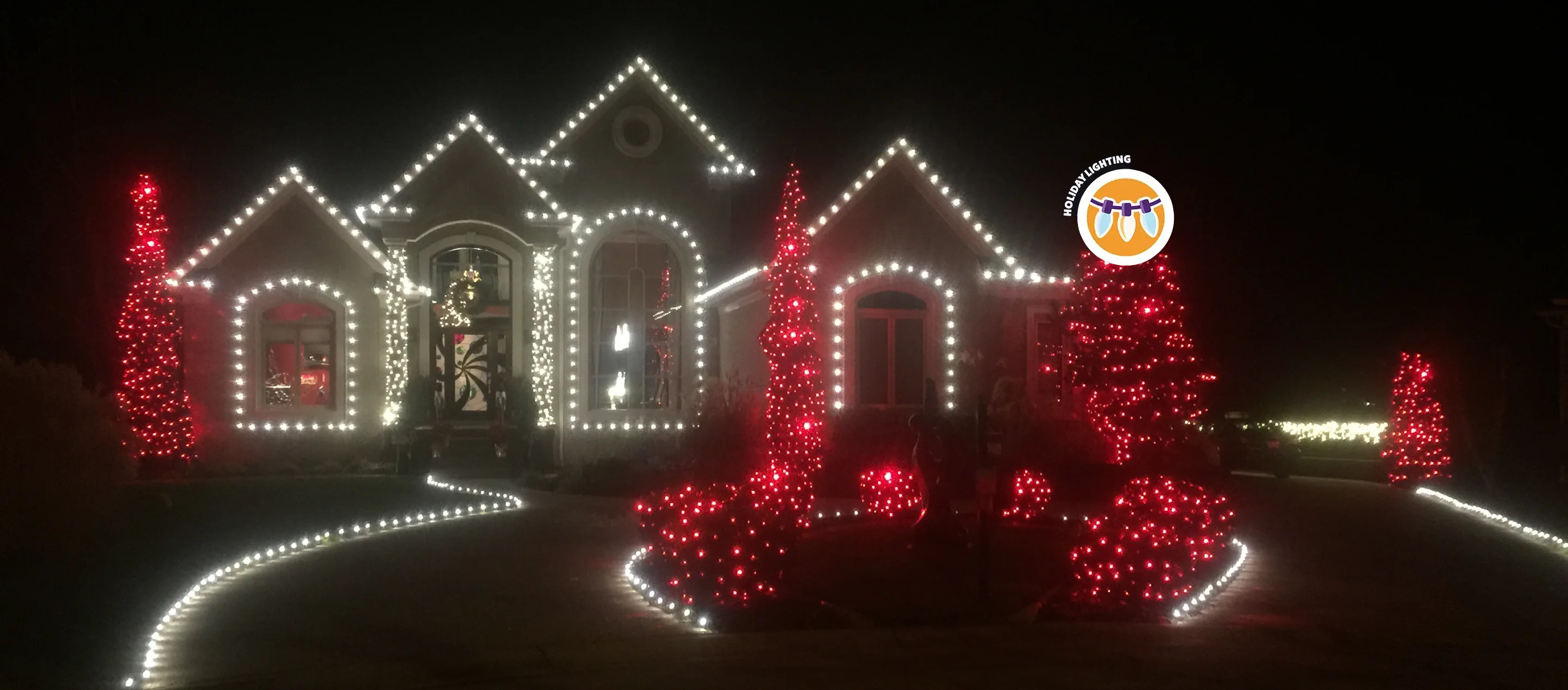 Large single-family home with wraparound driveway lit up by red and white holiday lights.