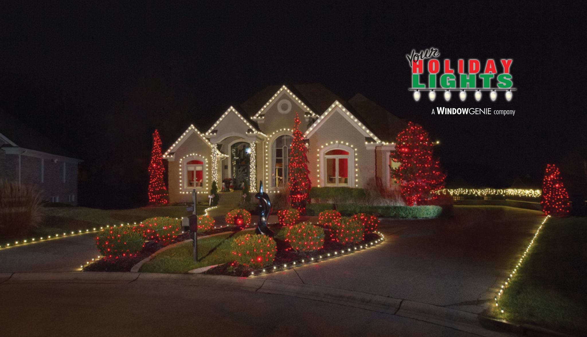 Large single-family home with wraparound driveway lit up by red and white holiday lights.