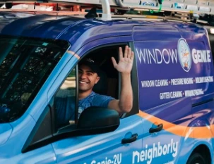 Window Genie tech waving while driving the company van to a commercial window cleaning job