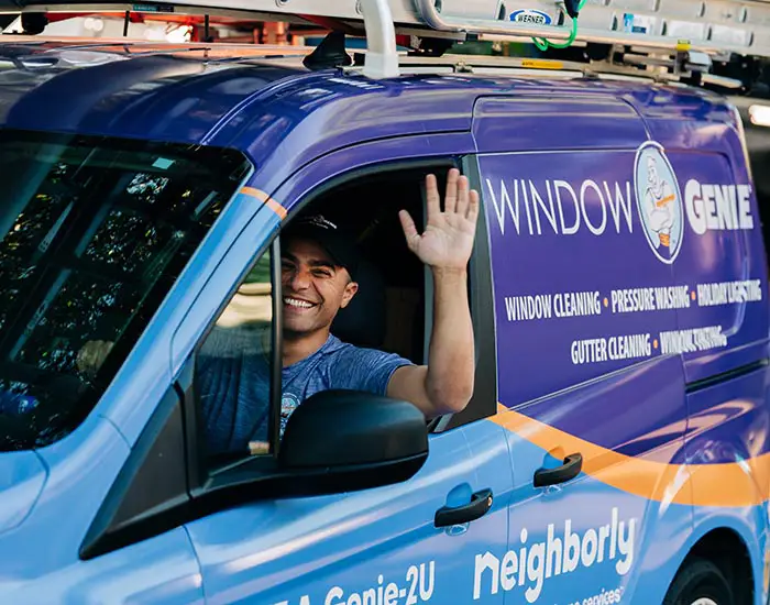  Window Genie tech waving while driving company van to a commercial window cleaning job.