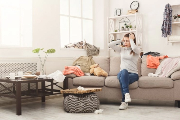 Woman sitting in messy living room.