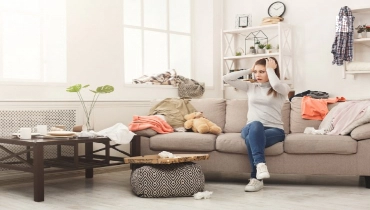 Woman sitting in messy living room.